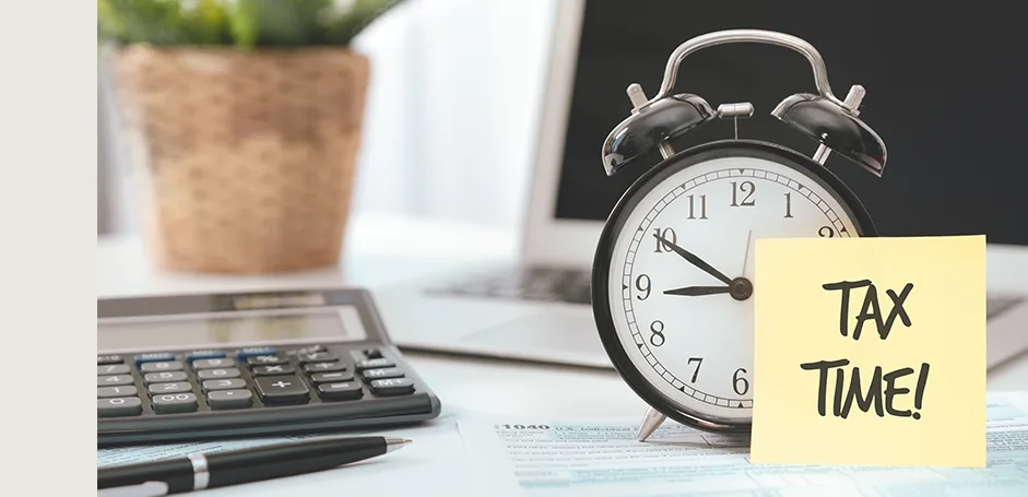 Alarm clock with a 'Tax Time!' sticky note beside a calculator