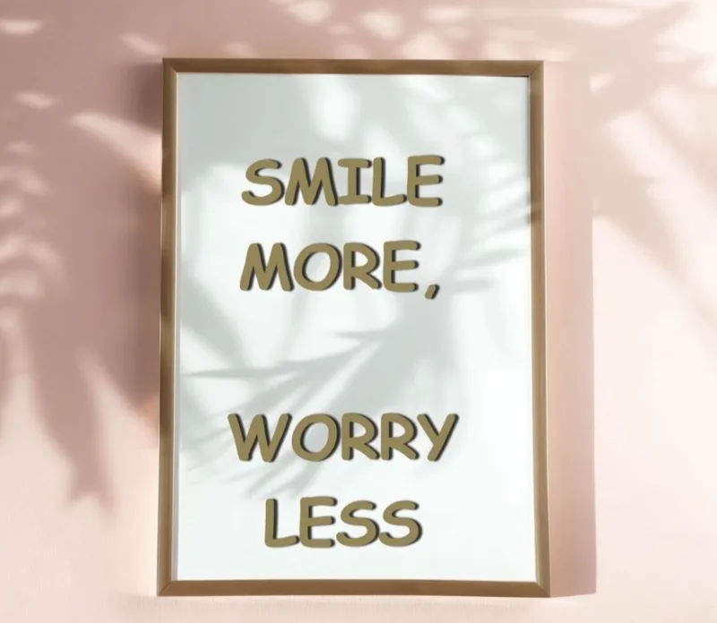 Framed print on a pink wall reading 'Smile more, worry less'